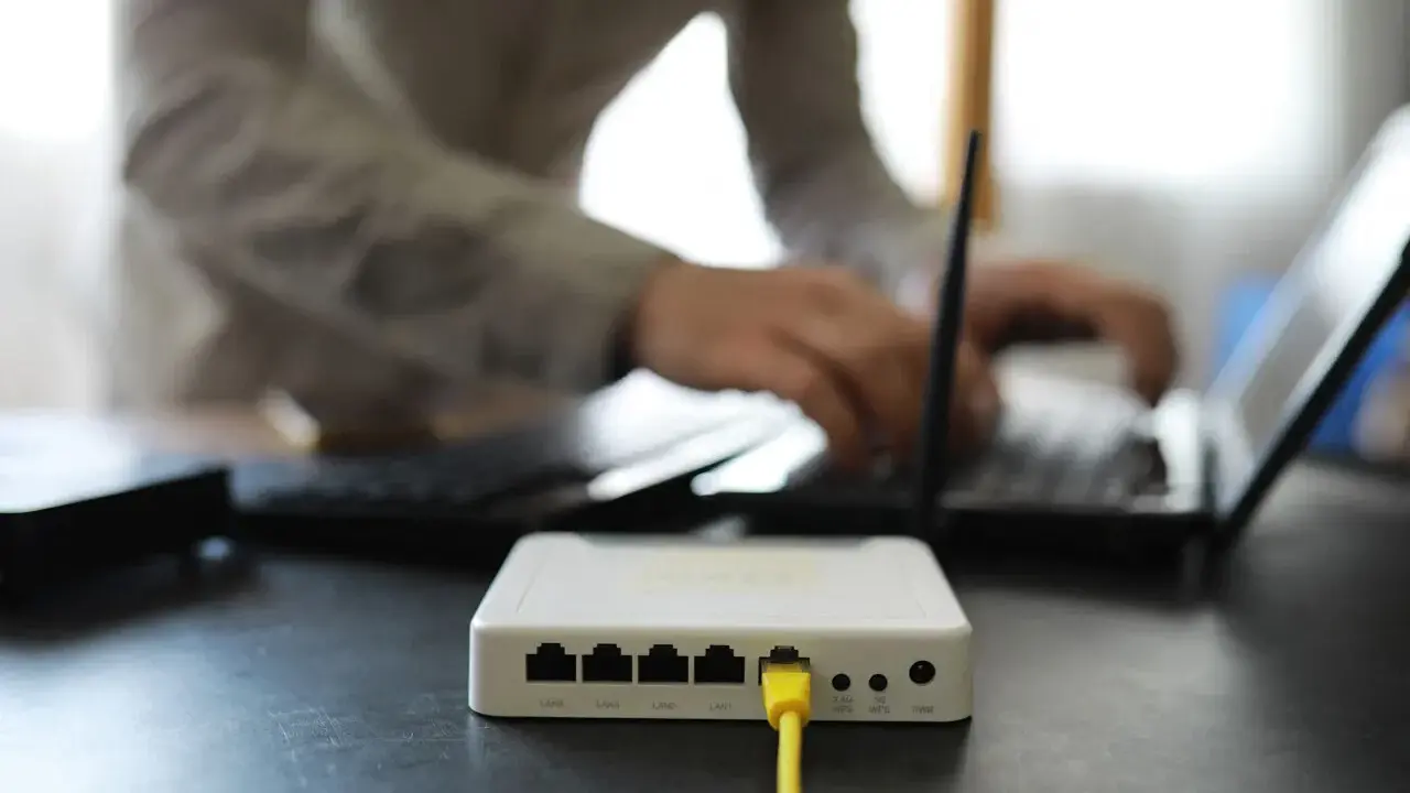 Connexion internet : faut il mettre les espaces pour la clé wifi ? Un routeur blanc est branché, une personne tape sur un ordinateur portable.