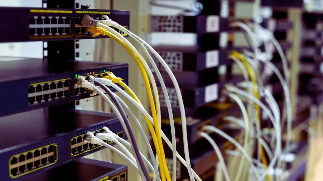 Faisceau de câblage RJ45 b, avec des câbles blancs, jaunes et gris connectés à des commutateurs réseau empilés.