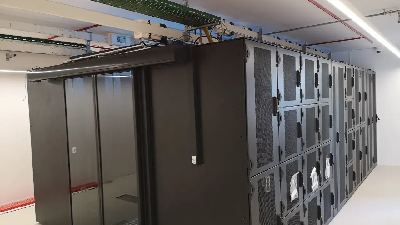 Un micro data center avec des baies de serveurs noires et une porte vitrée. Des câbles et des conduits sont visibles au plafond.
