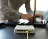 Connexion internet : faut il mettre les espaces pour la clé wifi ? Un routeur blanc est branché, une personne tape sur un ordinateur portable.