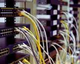 Faisceau de câblage RJ45 b, avec des câbles blancs, jaunes et gris connectés à des commutateurs réseau empilés.
