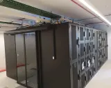 Un micro data center avec des baies de serveurs noires et une porte vitrée. Des câbles et des conduits sont visibles au plafond.