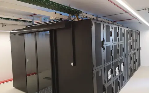 Un micro data center avec des baies de serveurs noires et une porte vitrée. Des câbles et des conduits sont visibles au plafond.