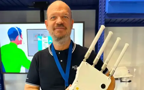 Un homme souriant tient un appareil avec quatre antennes, prêt à optimiser votre reseau wifi.