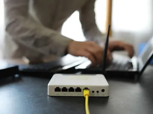 Connexion internet : faut il mettre les espaces pour la clé wifi ? Un routeur blanc est branché, une personne tape sur un ordinateur portable.