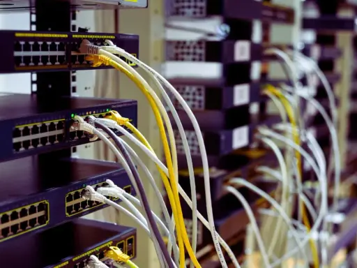 Faisceau de câblage RJ45 b, avec des câbles blancs, jaunes et gris connectés à des commutateurs réseau empilés.