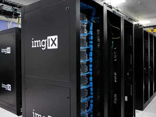 Des racks de serveurs noirs, dont un avec le logo "imgIX", remplis de câbles bleus et jaunes. C'est un peu ça, un serveur : le cœur de l'internet.