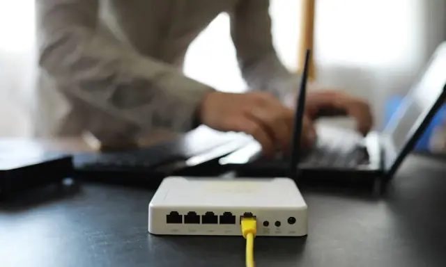 Connexion internet : faut il mettre les espaces pour la clé wifi ? Un routeur blanc est branché, une personne tape sur un ordinateur portable.