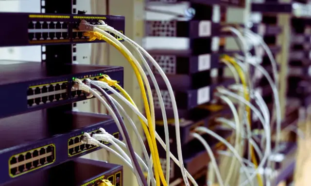 Faisceau de câblage RJ45 b, avec des câbles blancs, jaunes et gris connectés à des commutateurs réseau empilés.