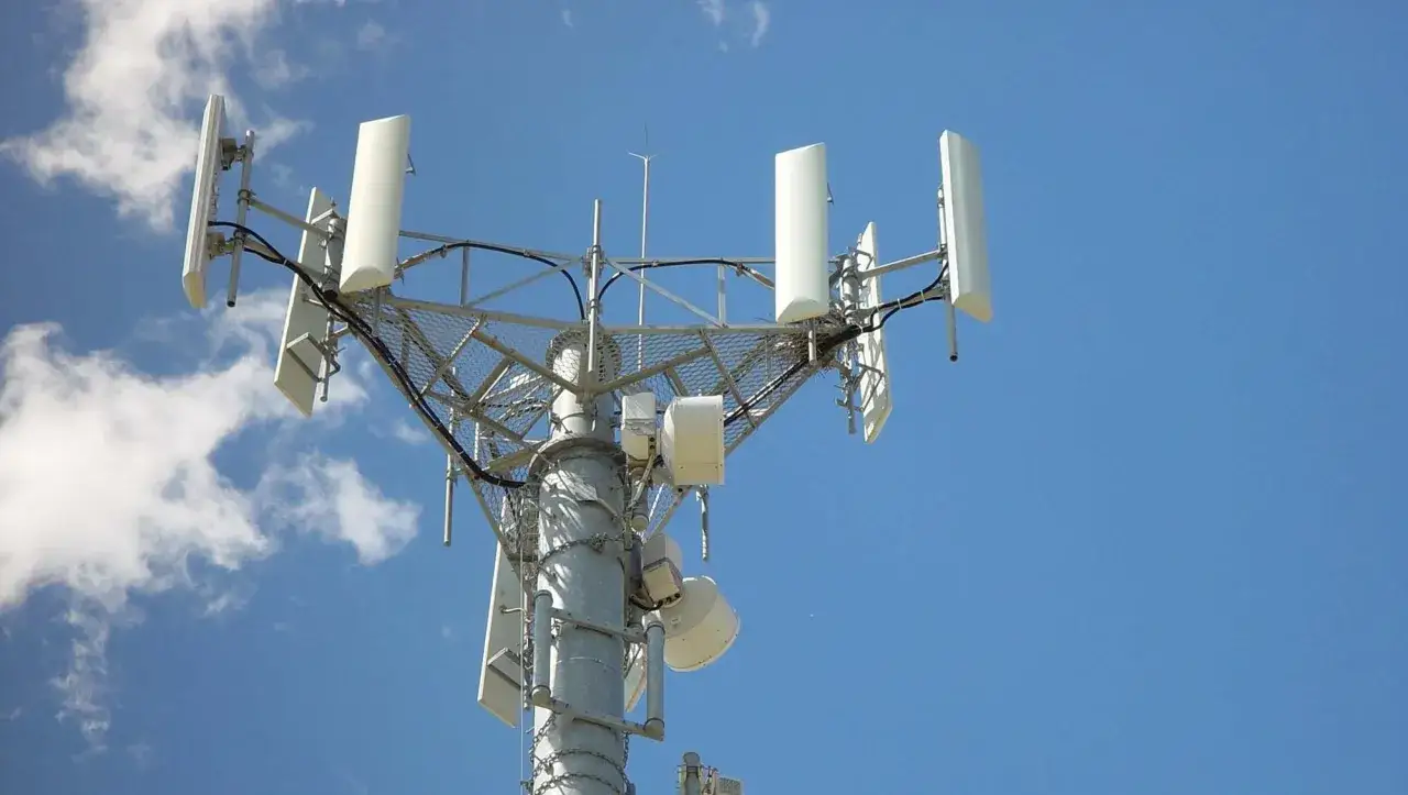Antenne de télécommunication pour le réseau 3G, avec des panneaux blancs et une structure métallique sous un ciel bleu et nuageux.