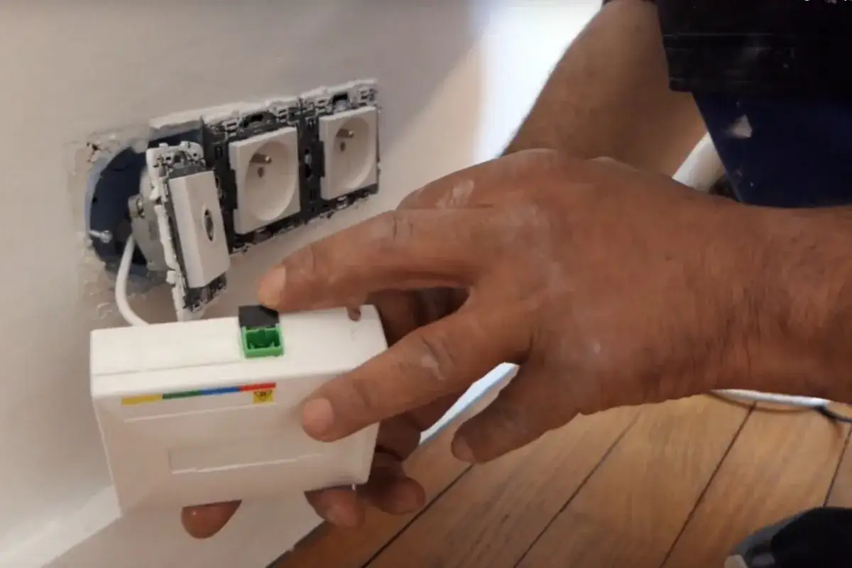Installation d'une prise fibre optique Free. Un technicien connecte un boîtier blanc à une prise murale.