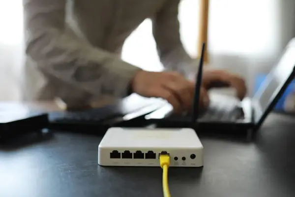 Connexion internet : faut il mettre les espaces pour la clé wifi ? Un routeur blanc est branché, une personne tape sur un ordinateur portable.